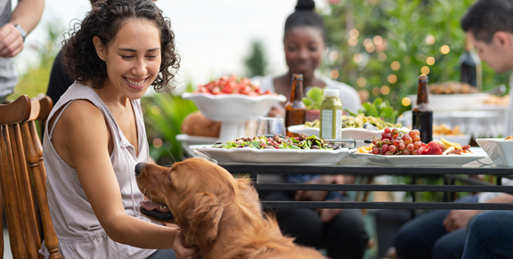 Women petting dog while eating food at lunch outside.
